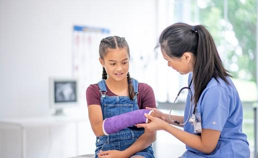 A doctor looking at a girl's arm cast.
